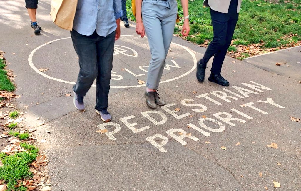 three people walk through a pedestrian priority sign