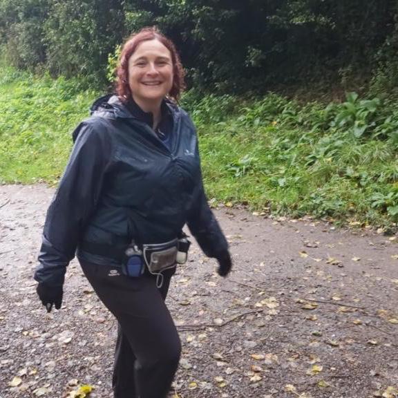 Catherine on a virtual walking marathon, she is smiling and looking into the camera as she walks along a path