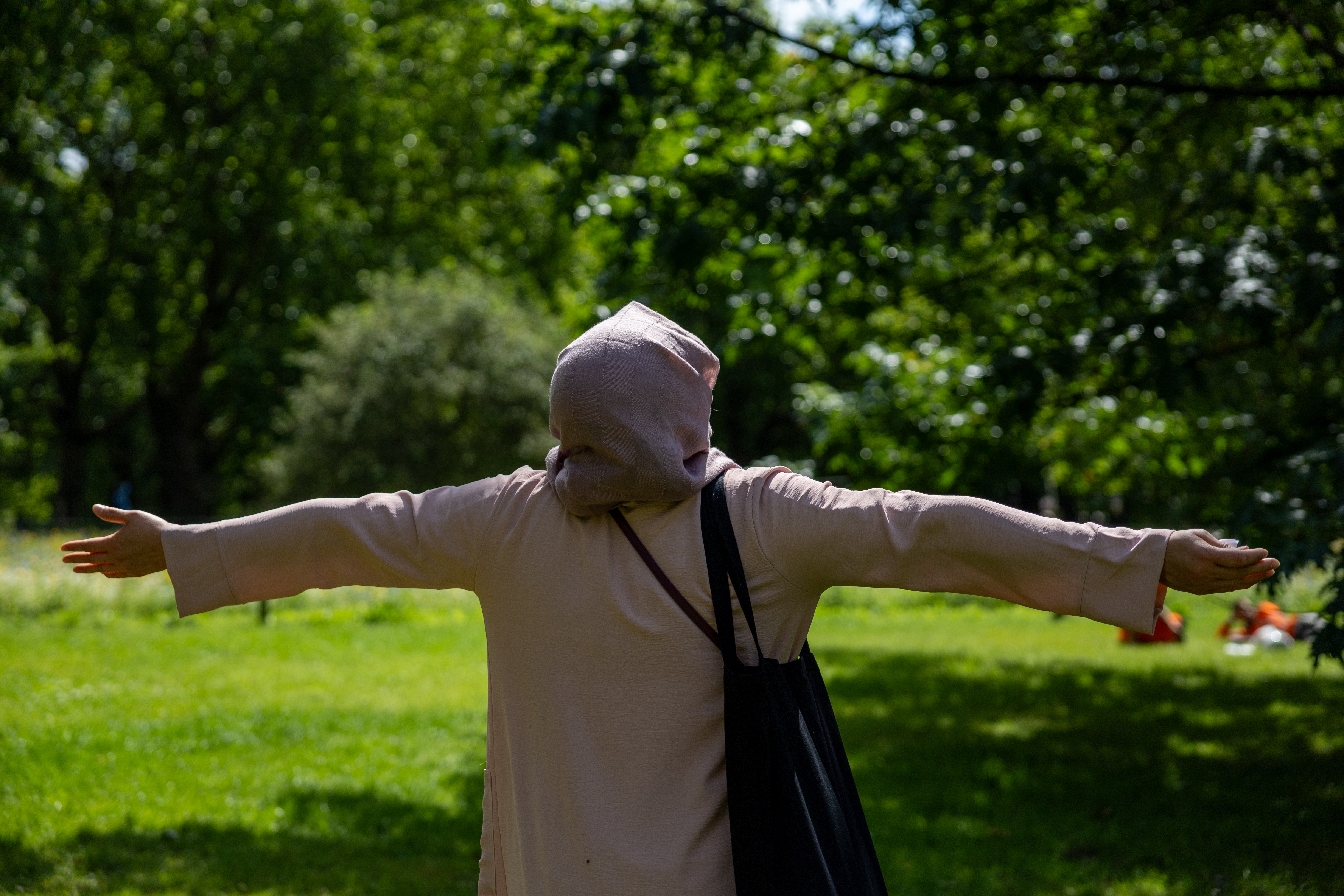 A woman stands in a park with her arms outstretched