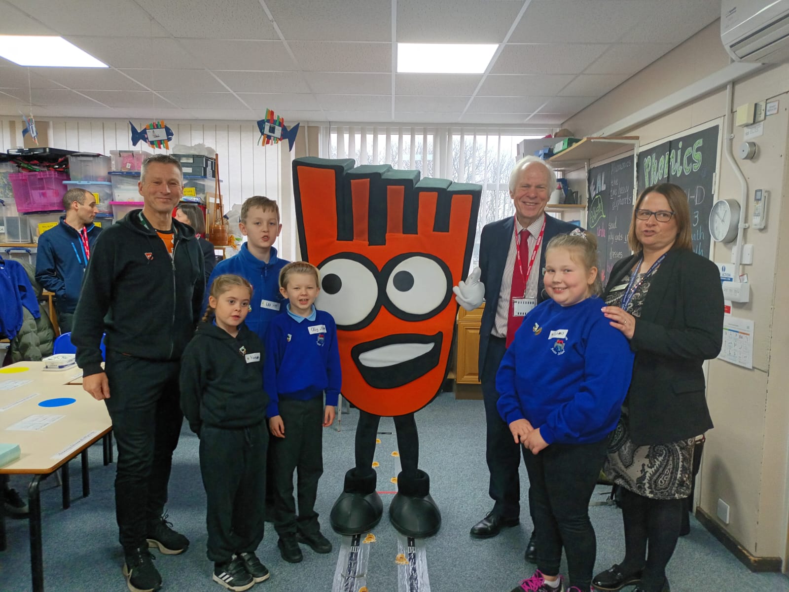 A photo of Sir Nic Dakin with pupils, school staff and Strider - a large foot mascot