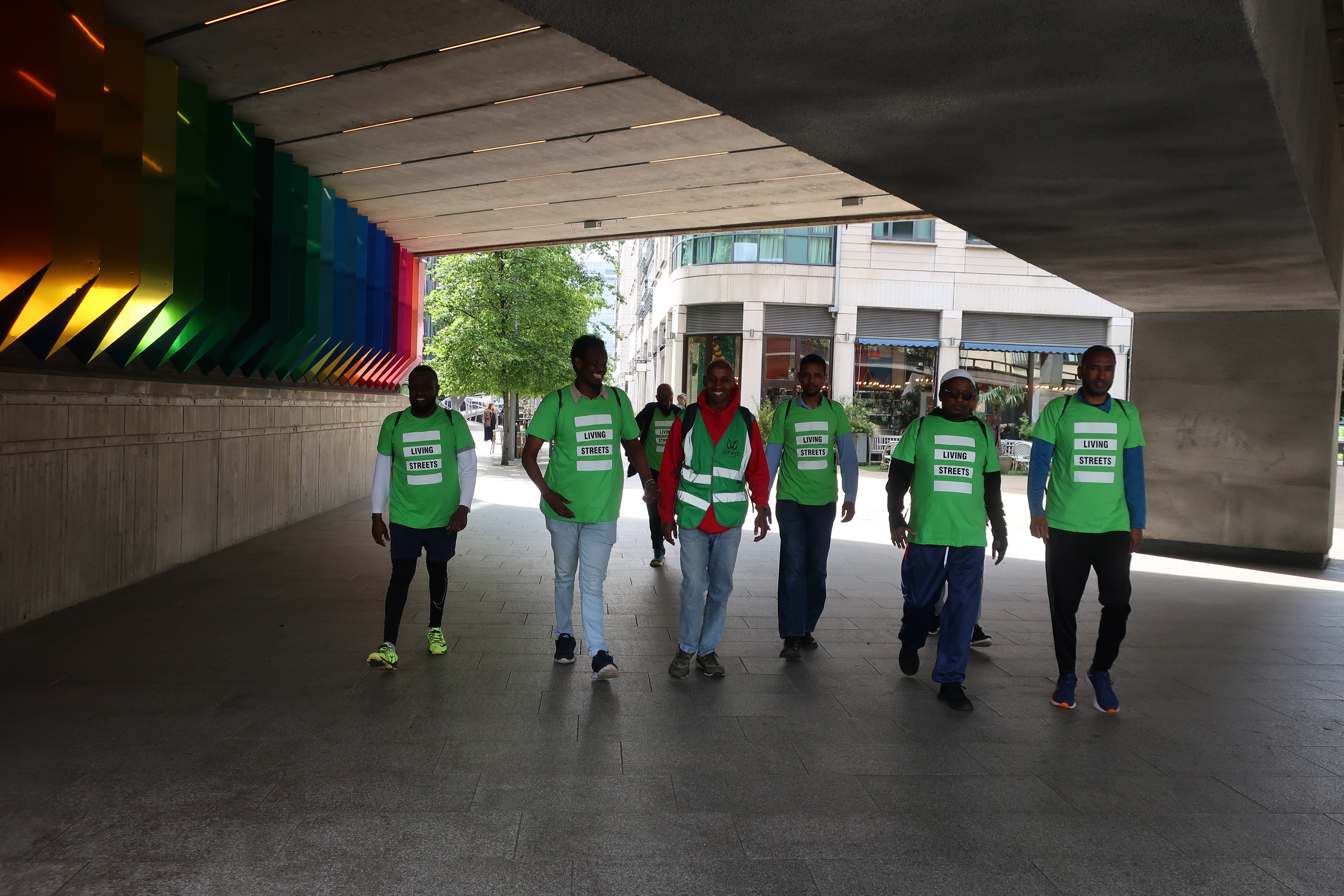 A group of men smiling walk underneath an underpass wearing green living streets tshirtd
