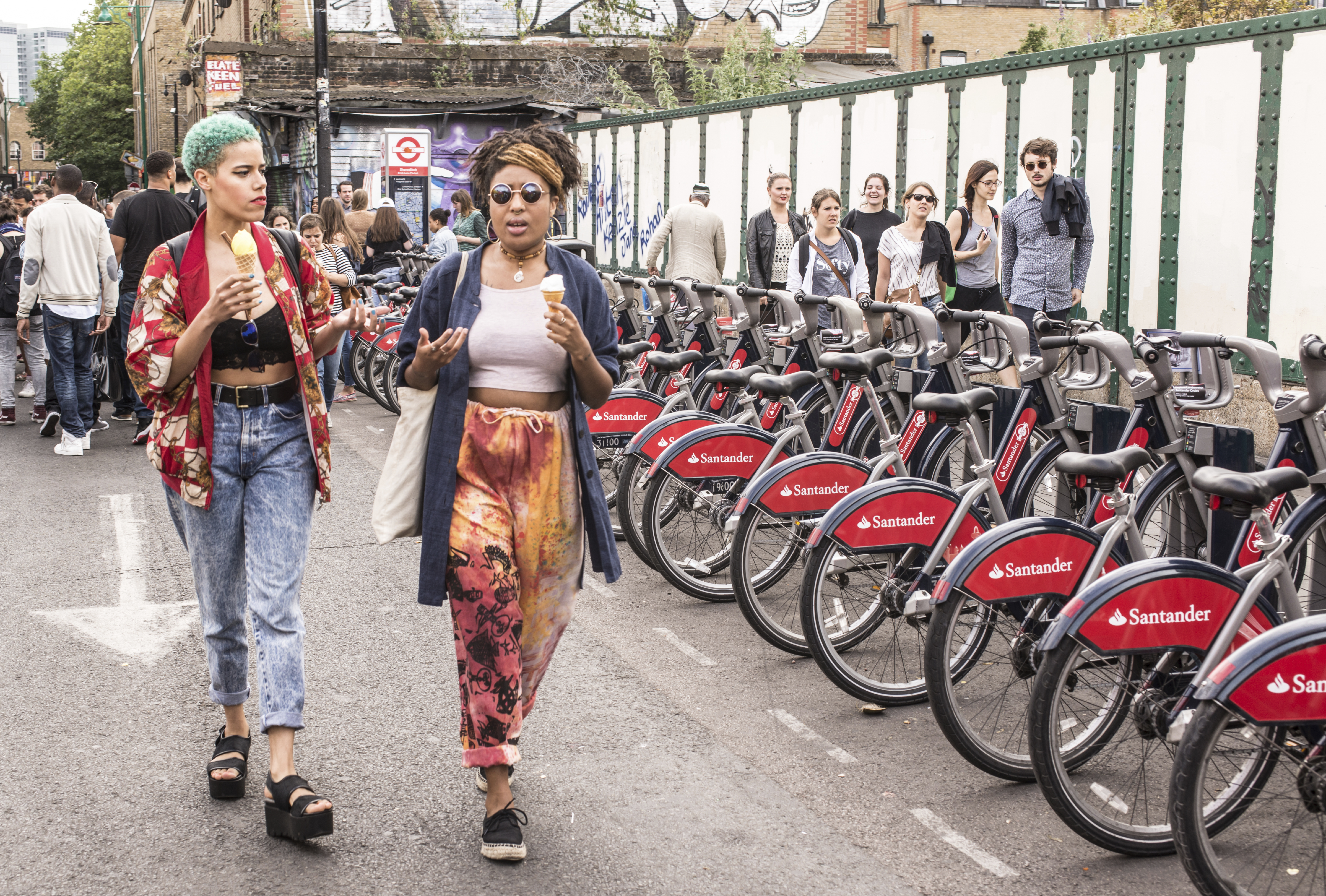 two black women walk past some ebikes in East London