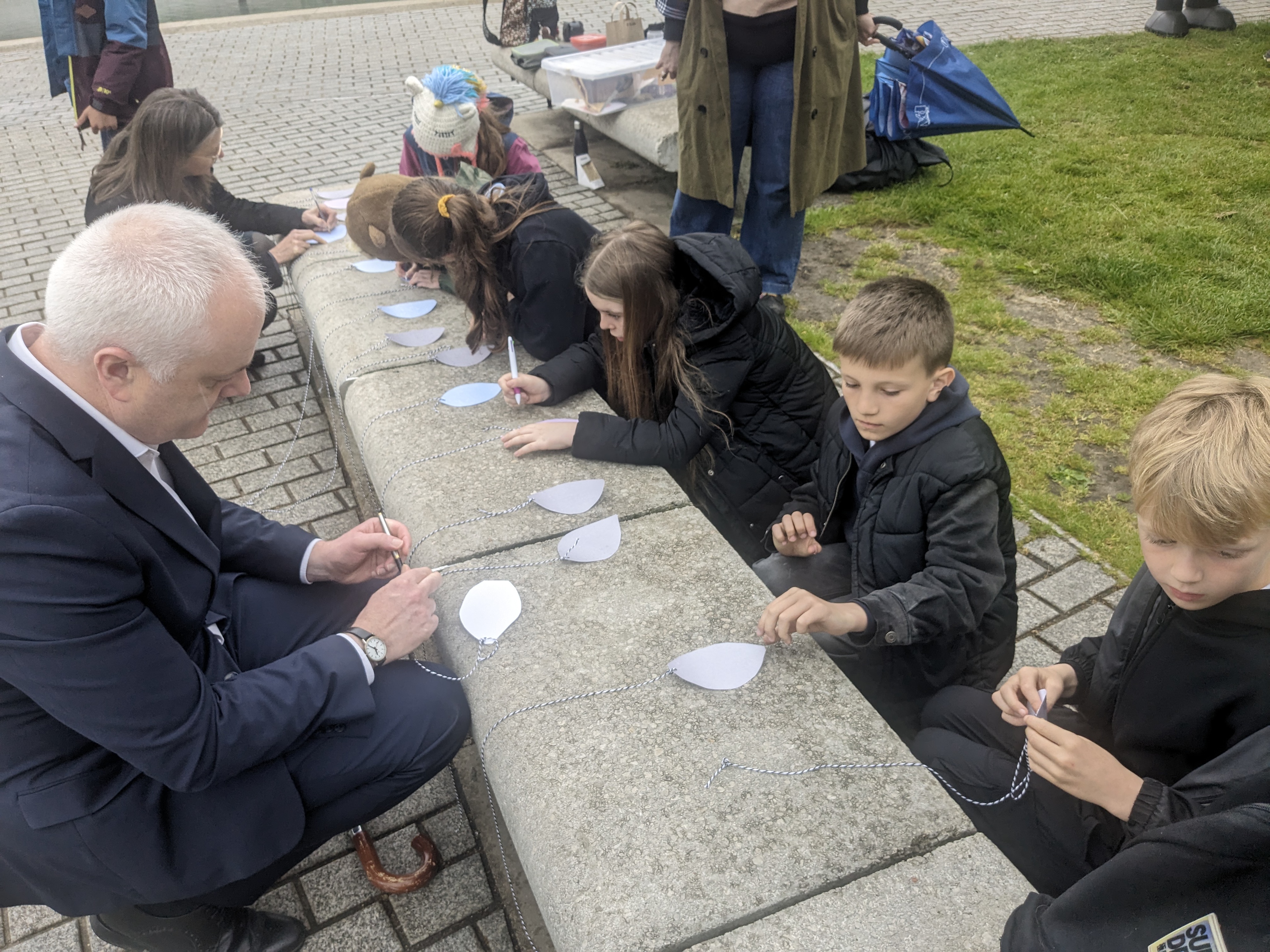 MSPS and pupils crouch at a stone bench writing on paper leaves