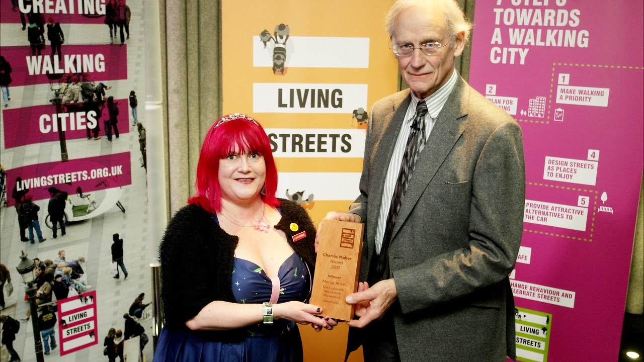 Morag is standing next to a man and they are both holding a wooden plaque