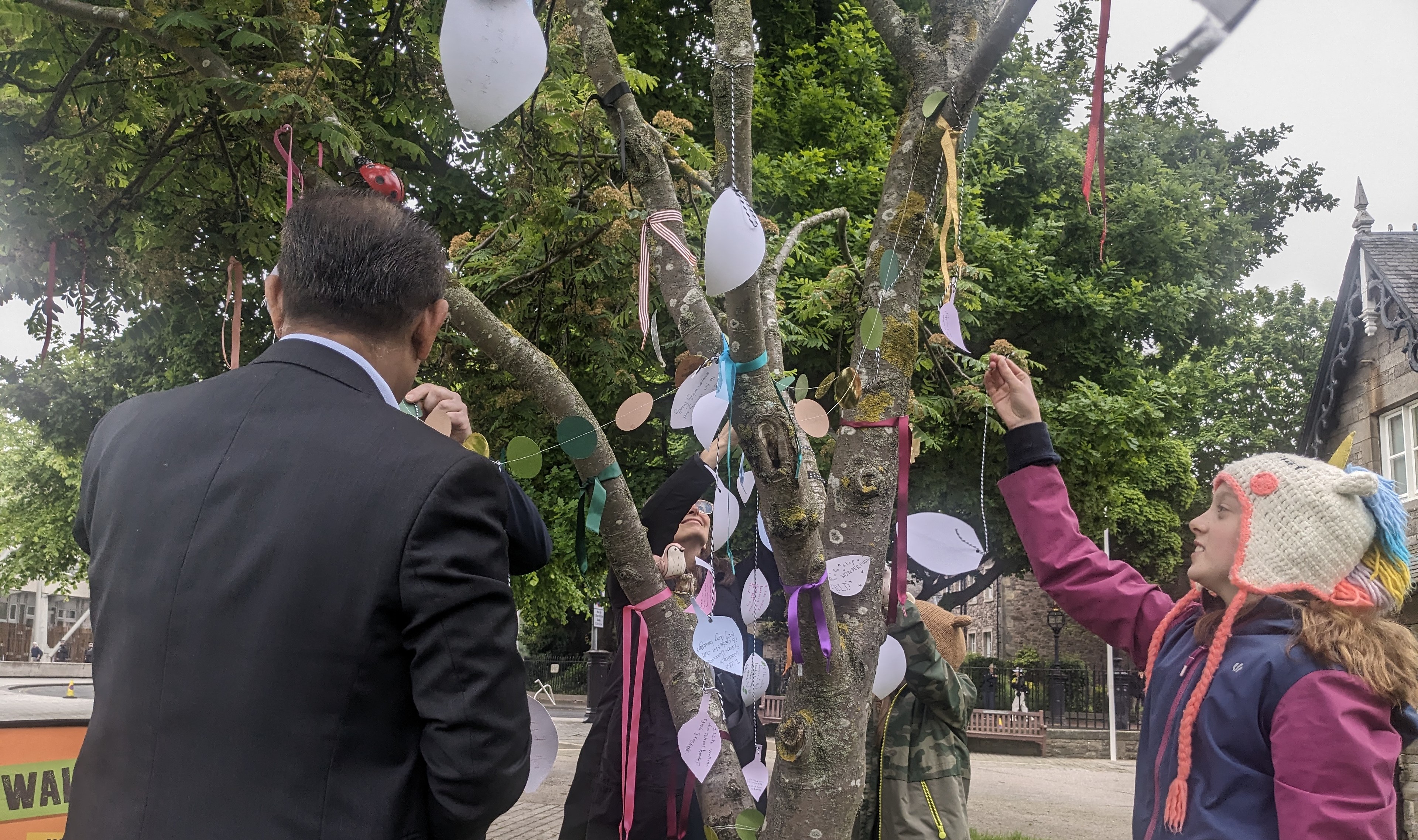 MSPs and pupils hang paper leaves from a tree